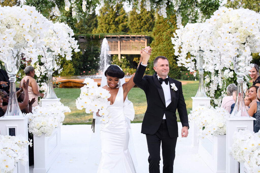 Bride and groom walking down aisle holding hands in the air outside at the Chicago Botanic Garden